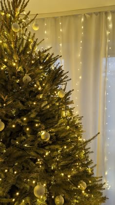 a christmas tree with lights and ornaments in front of a window