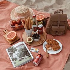 an open book and some food on a blanket near a bag with a straw hat