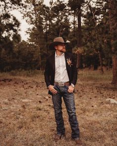 a man standing in the middle of a field wearing a cowboy hat and blue jeans