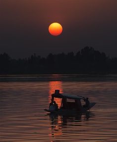 a small boat floating on top of a lake under a bright orange sun in the sky