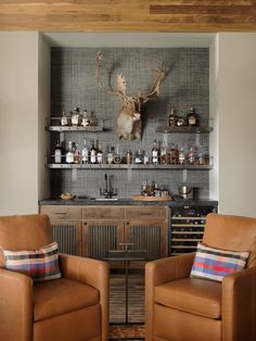 two leather chairs in front of a bar with deer heads on the wall behind them