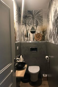 a toilet and sink in a small room with palm tree wallpaper on the walls