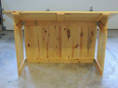 a table made out of wooden planks in a room with concrete flooring and white walls