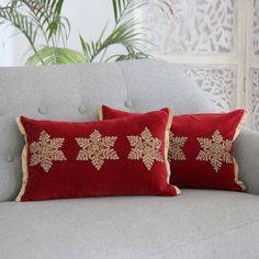 two red pillows sitting on top of a gray couch next to a potted plant