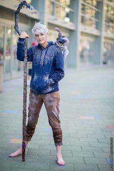 an older woman with white hair and blue shirt holding a snake in her hands while standing on the sidewalk