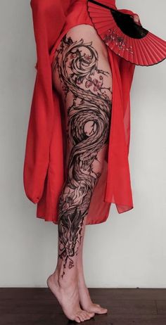 a woman with tattoos on her leg holding a fan and wearing a red kimono