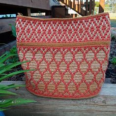 an orange and beige purse sitting on top of a wooden table next to plants in a garden