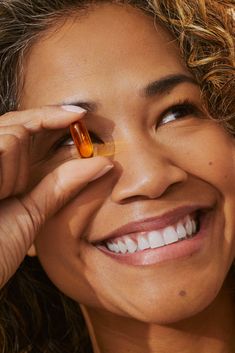 a woman smiling and holding an orange pill in her right hand