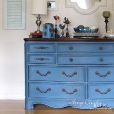 a blue dresser with pictures on the wall and a mirror above it, in front of a white wall