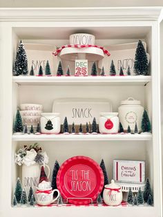 a white hutch with christmas decorations and dishes on the top shelf, including plates