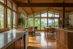 an open kitchen and living room area with wood flooring, large windows, and wooden furniture