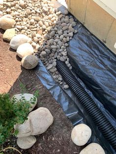 a black hose is laying on the ground next to some rocks and gravel in front of a house