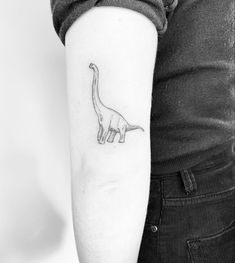 a black and white photo of a small dinosaur tattoo on the left upper arm,