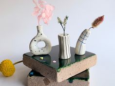 three vases with flowers in them sitting on top of a piece of concrete,