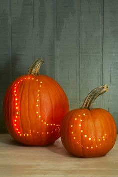 two orange pumpkins sitting next to each other on top of a wooden table in front of a wall