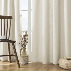 a white vase with flowers in it sitting next to a wooden chair and window sill