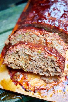 sliced meatloaf with sauce on it sitting on top of a wooden cutting board