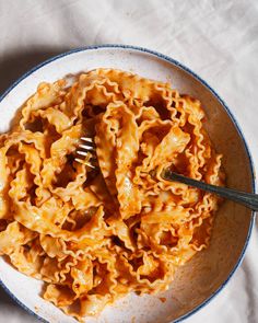 a white bowl filled with pasta on top of a table next to a knife and fork