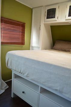 a white bed sitting in a bedroom next to a window with blinds on top of it