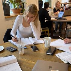 two women sitting at a table with notebooks and papers in front of them, working on laptop computers