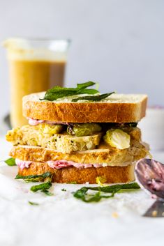 two sandwiches stacked on top of each other next to a cup of coffee and a spoon