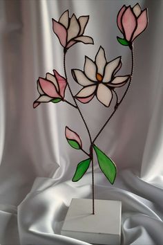 a stained glass flower with green leaves on a white base, sitting on a satin background