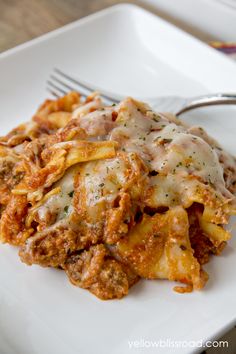 a white plate topped with lasagna covered in sauce and cheese next to a fork