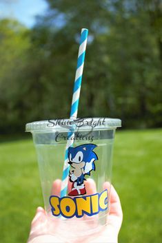 someone holding up a plastic cup with a blue and white striped straw in front of them