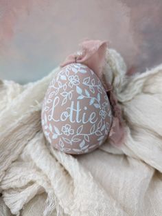 an easter egg with the word ottie painted on it sitting on a white blanket