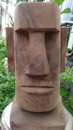 a wooden sculpture sitting on top of a metal stand in front of some bushes and trees