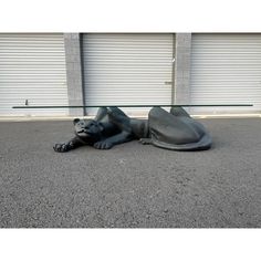 a statue of a dog laying on the ground in front of a garage door with roller doors behind it