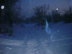 a person riding skis down a snow covered slope at night with trees in the background