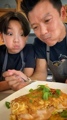 a man and child are looking at a plate of food on the table with chopsticks in front of them