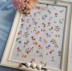 a white frame with flowers on it next to some beads and pink carnations