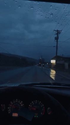 rain is falling on the windshield of a car as it drives down a road at night