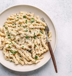 a white plate topped with macaroni and cheese covered in parsley next to a fork