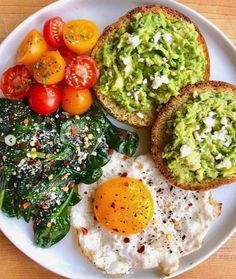 a white plate topped with eggs, spinach and tomatoes next to toasted bread