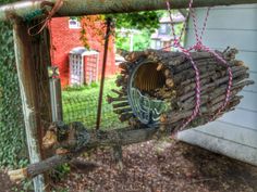 a birdhouse made out of branches and logs on a tree branch in front of a house