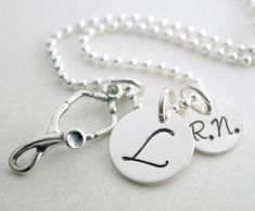 "RN Graduation Necklace Gift - Personalized Nurse Necklace RN Graduation Custom Jewelry Hand Stamped Sterling Silver Custom Nurse Necklace The 1/2\" sterling silver disc is hand stamped with the initial of your choice. The 3/8\" disc is hand stamped with the abbreviation \"R.N.\". Hanging with the name charms is a sterling silver stethoscope charm. This necklace comes on an 18\" sterling silver bead chain. If you would like to inquire about other chain options, please convo us prior to placing y Sterling Silver Hand Stamped Round Disc Necklace, Sterling Silver Pendant Jewelry, Hand Stamped Sterling Silver Round Pendant Necklace, Sterling Silver Necklace For Personal Use, Sterling Silver Dog Tag Necklace With Charms, Silver Stamped Round Disc Charm Necklace, Silver Hand Stamped Pendant Charm Necklace, Silver Medallion Necklace Hand Stamped, Adjustable Hand Stamped Silver Necklace