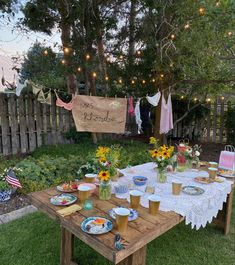 a table with plates and cups on it in the grass next to a wooden fence