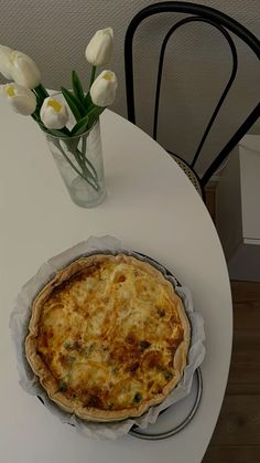 a white table topped with a pie next to a vase filled with flowers