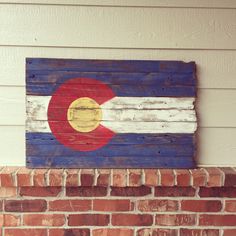 a wooden sign with the flag of colorado painted on it's side next to a brick wall