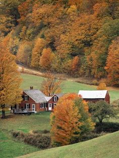 a red house surrounded by trees with fall foliage on the hillsides in the background