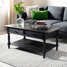 a black coffee table sitting on top of a white rug next to a gray couch