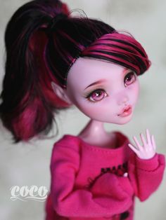 a close up of a doll wearing a pink shirt and black hair with her hand on her hip