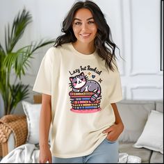 Elevate your casual wardrobe with the Comfort Colors 1717 "Adorable Cat on Books" T-shirt. Made from 100% ring-spun US cotton, this garment-dyed, soft-washed tee offers unparalleled comfort and style. The relaxed fit is perfect for everyday wear, while the durable double-needle stitching and tubular design ensure long-lasting quality. Featuring a cute cat lounging on a stack of books, this tee is perfect for book lovers and cat enthusiasts alike. Available in 58 vibrant colors, this pre-shrunk, Bookish Crew Neck T-shirt With Funny Print, Bookish Crew Neck Top With Character Print, Cat Lounging, Book Tshirts, Stack Of Books, Daughter Gifts, Casual Wardrobe, Mom Gift, Tshirt Colors