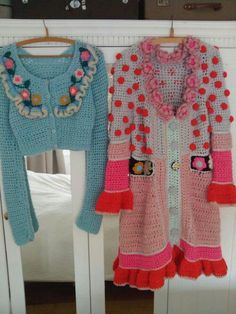 two crocheted sweaters are hanging on a clothes rack next to a bed