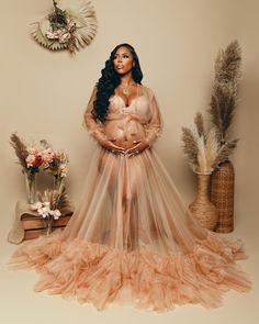 a pregnant woman standing in front of a wall with flowers and feathers on the floor