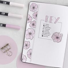 an open notebook with pink flowers on it next to two pens and a pair of eyeglasses