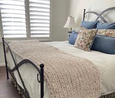 a bed with white sheets and blue pillows in a bedroom next to a window that has shutters